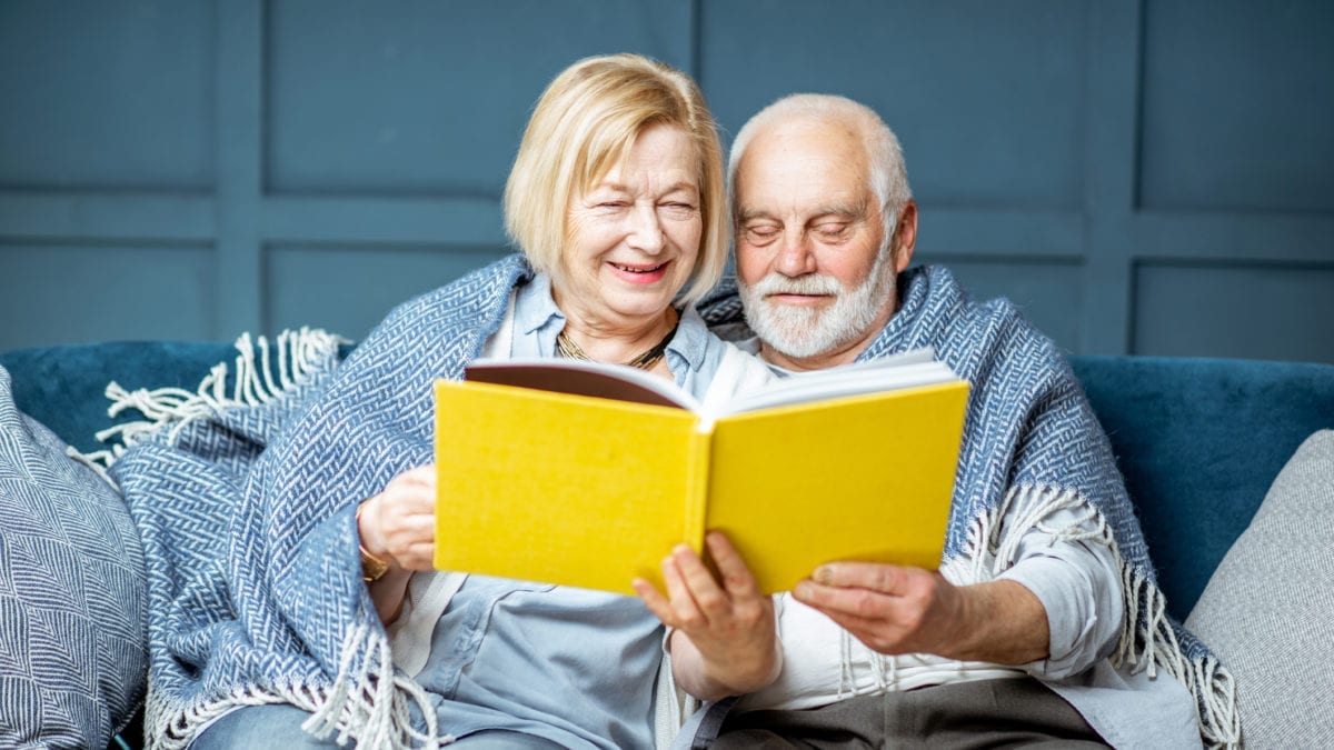 Senior Couple Reading Book On The Couch At Home